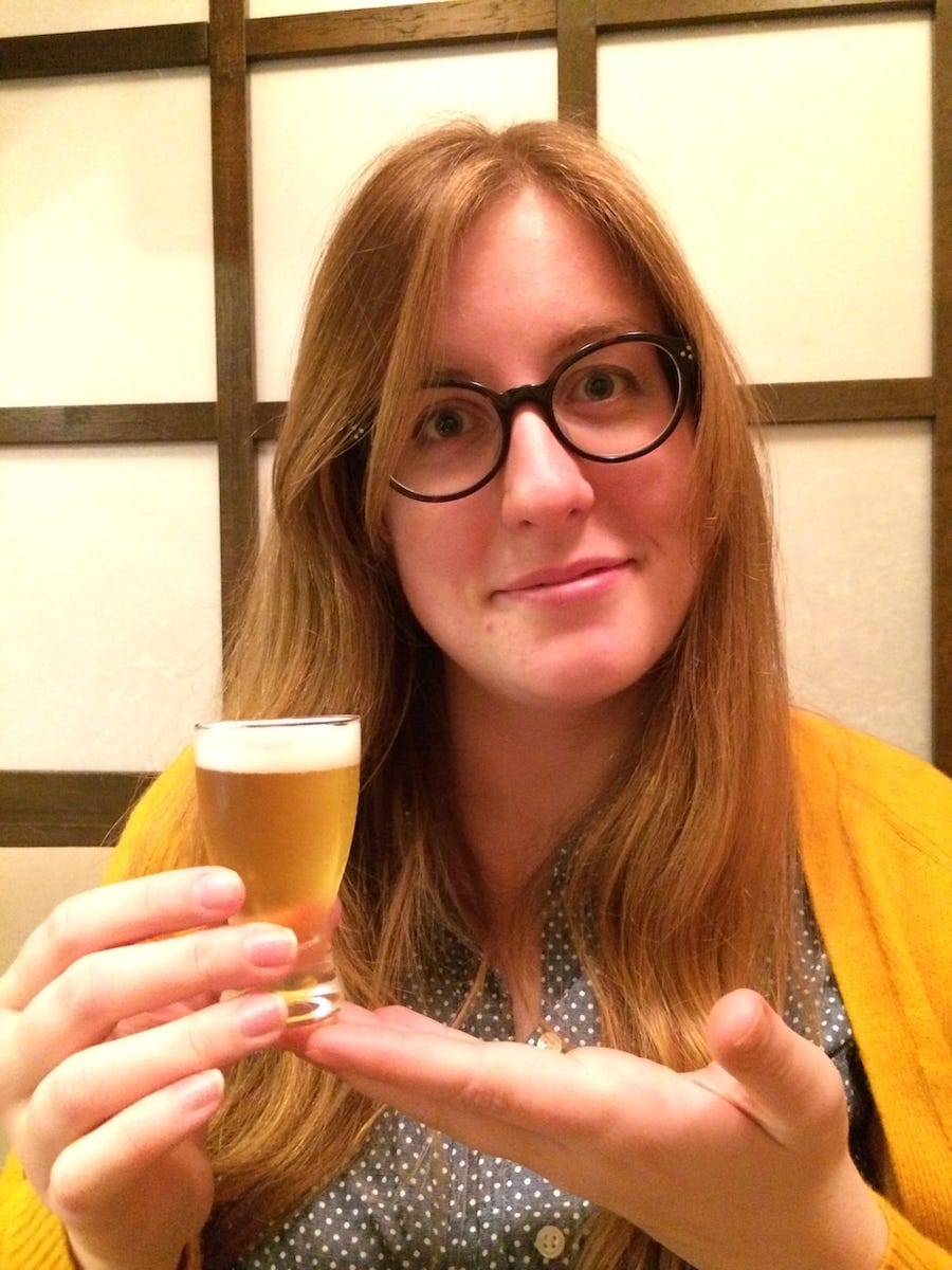 A photograph of a woman, Erin, presenting her unusually small glass of beer at a restaurant in Japan.